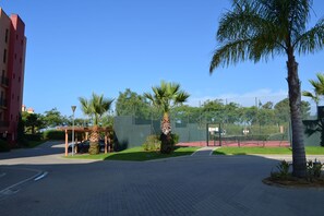 Ein gepflasterter Innenhof mit Palmen, einem Tennisplatz und einem roten Gebäude.