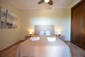 Une chambre à coucher avec un grand lit, deux lampes de chevet, un ventilateur de plafond et une armoire en bois.