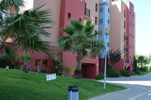 Ein mehrgeschossiges Wohngebäude mit roter und beiger Fassade, umgeben von gepflegtem Rasen und Palmen.