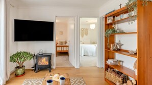 Un salon chaleureux avec un téléviseur, une cheminée, une bibliothèque et un lit à l’arrière-plan.