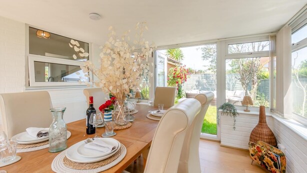Un coin repas avec une table en bois, des chaises blanches et un vase contenant des fleurs séchées.