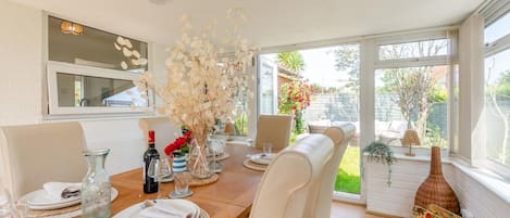 Un comedor con una mesa de madera, sillas blancas y un jarrón con flores secas.