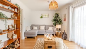 Un salon avec un canapé gris, des étagères en bois, un luminaire suspendu et une grande plante.
