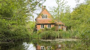 A house with a red roof, surrounded by dense greenery and a pond. - 2 Bed in Sibton (oc-q43760) (Sibton)