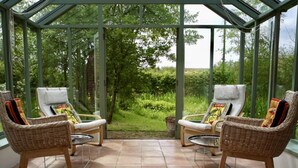 A conservatory with two wicker chairs, a small table, and a view of a garden. - 2 Bed in Sibton (oc-q43760) (Sibton)