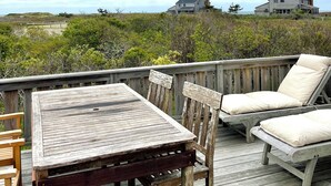 Une terrasse en bois avec une table et des chaises, donnant sur une zone verdoyante où l’on aperçoit des maisons au loin.