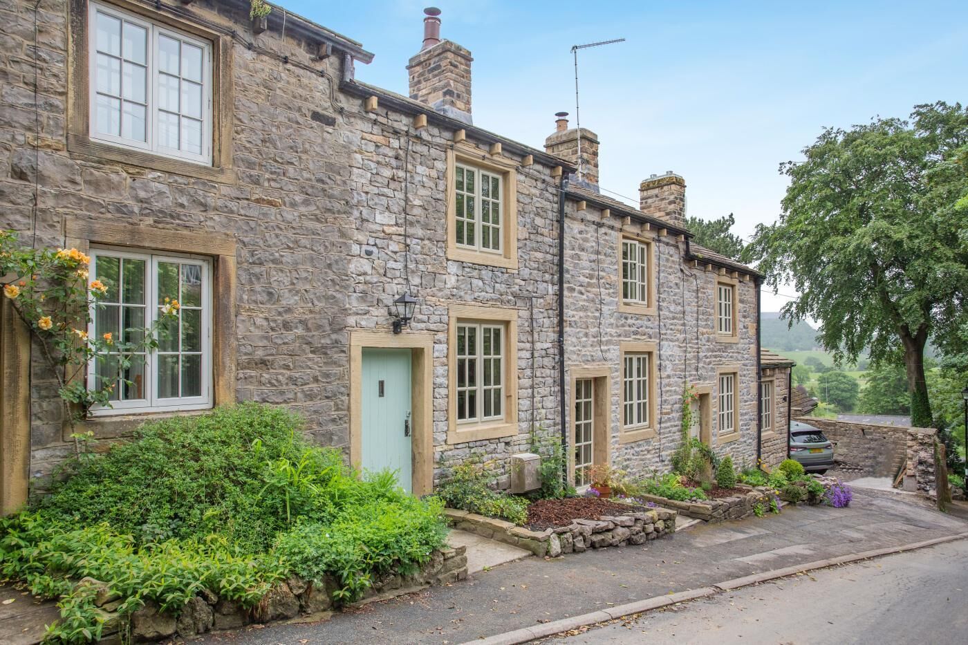 A stone house with multiple windows, a green door, and a car parked in front.