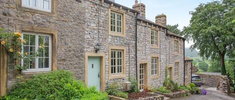 A stone house with multiple windows, a green door, and a car parked in front.