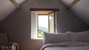 Ein Schlafzimmer mit schrägen Wänden, einem Fenster, einem Bett und einem Sessel.