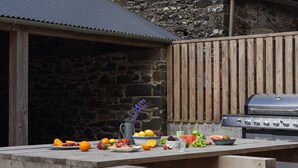 Ein Holztisch mit Obst und Gemüse, ein Grill und eine Steinwand.