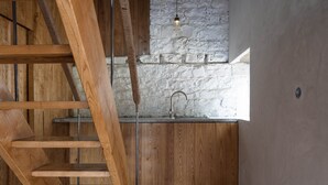 Eine Holztreppe führt zu einer Küche mit einer Steinwand und einer Pendelleuchte.