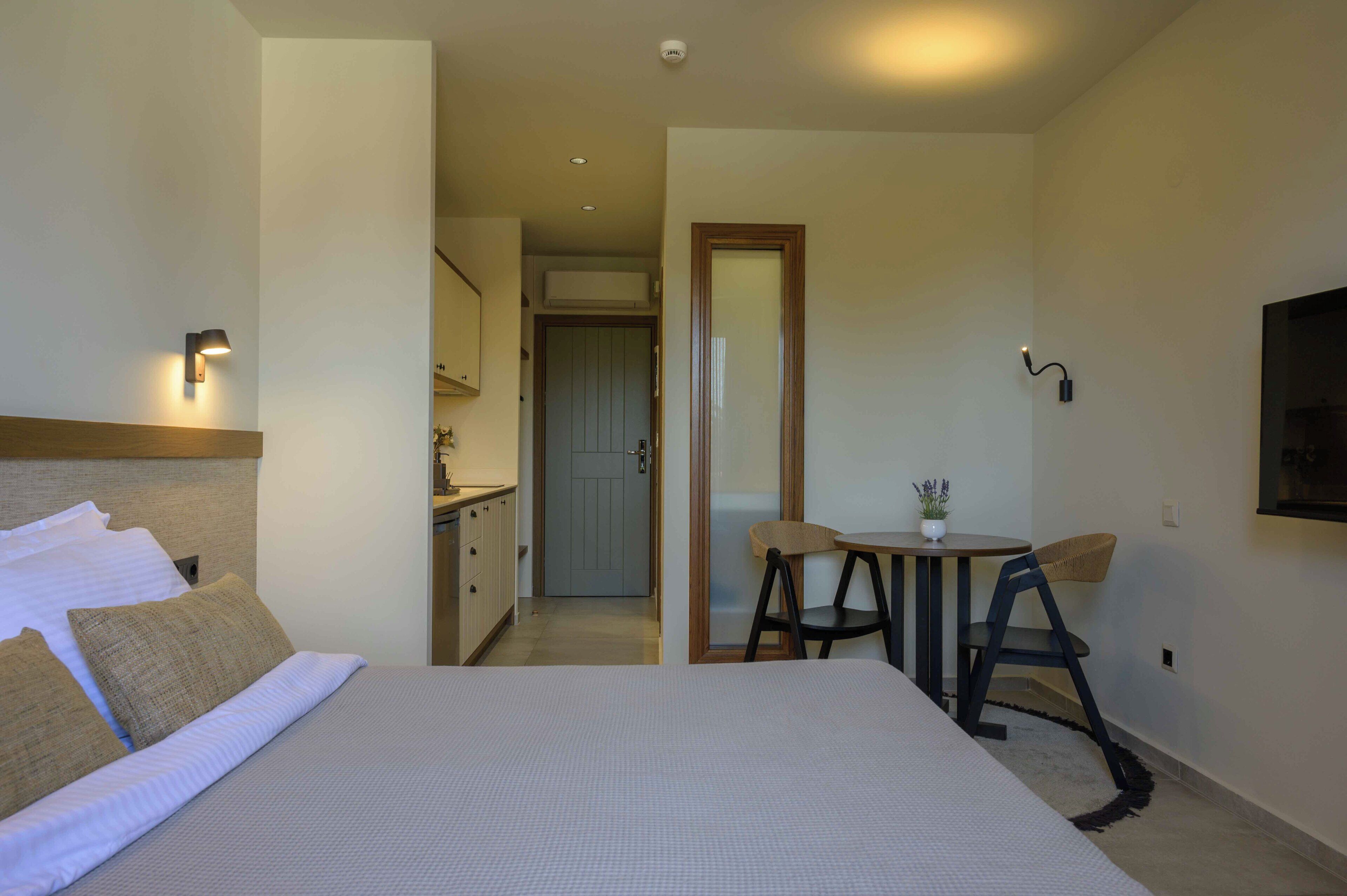 Quarto de hotel com uma cama, uma pequena mesa com uma cadeira, uma TV fixada na parede e uma porta que dá para um banheiro.