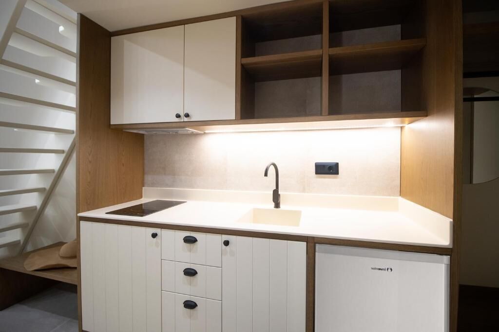A modern kitchen with white cabinetry, a built-in dishwasher, and a wooden staircase.