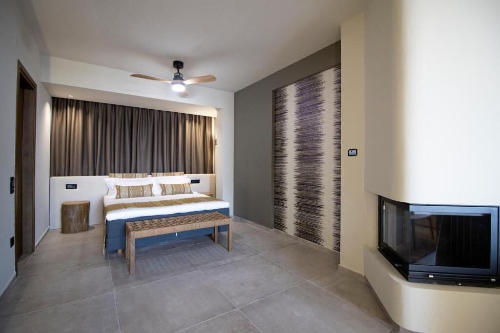 Une chambre à coucher moderne avec un lit, un banc, un ventilateur de plafond, une grande fenêtre et une cheminée.