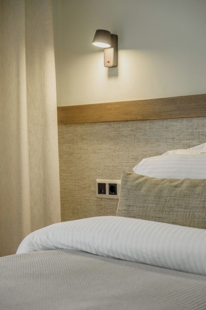 A hotel room with a bed, a wall-mounted light, and a power outlet.