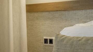A hotel room with a bed, a wall-mounted light, and a power outlet.