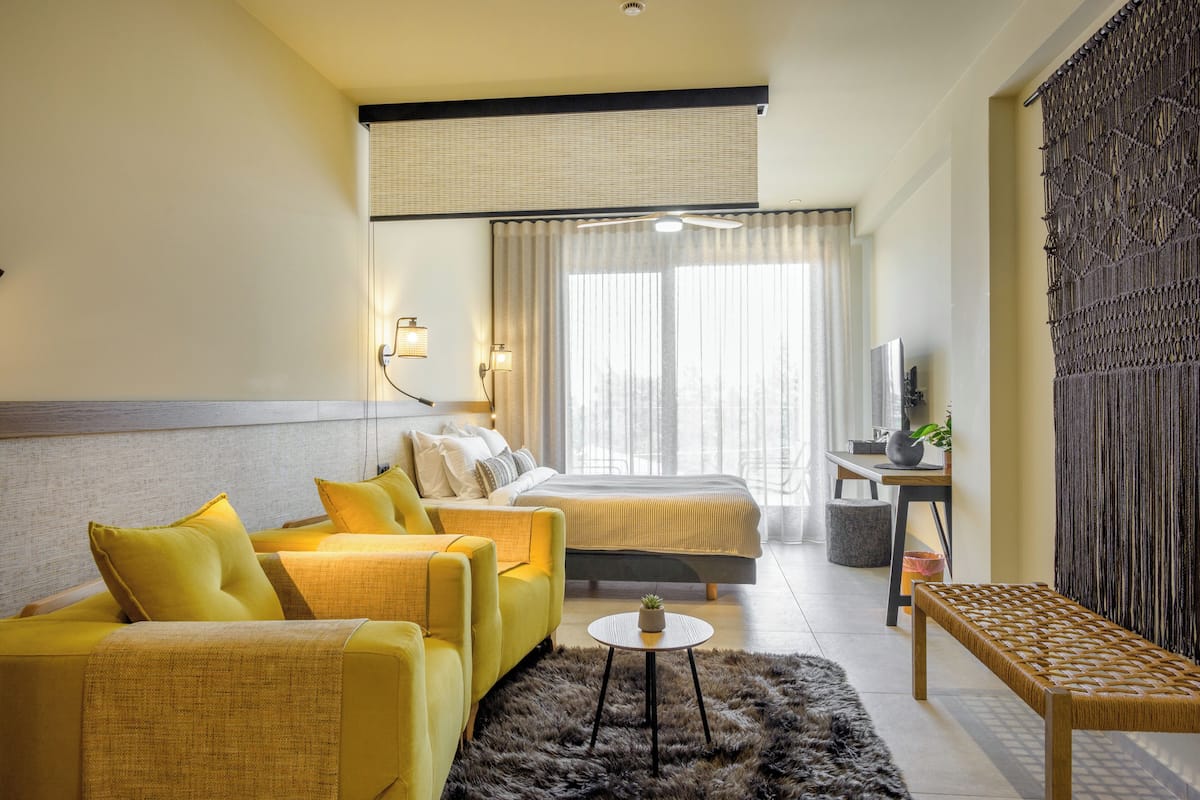 A hotel room with a bed, a sofa, a small table, a bench, and a TV.
