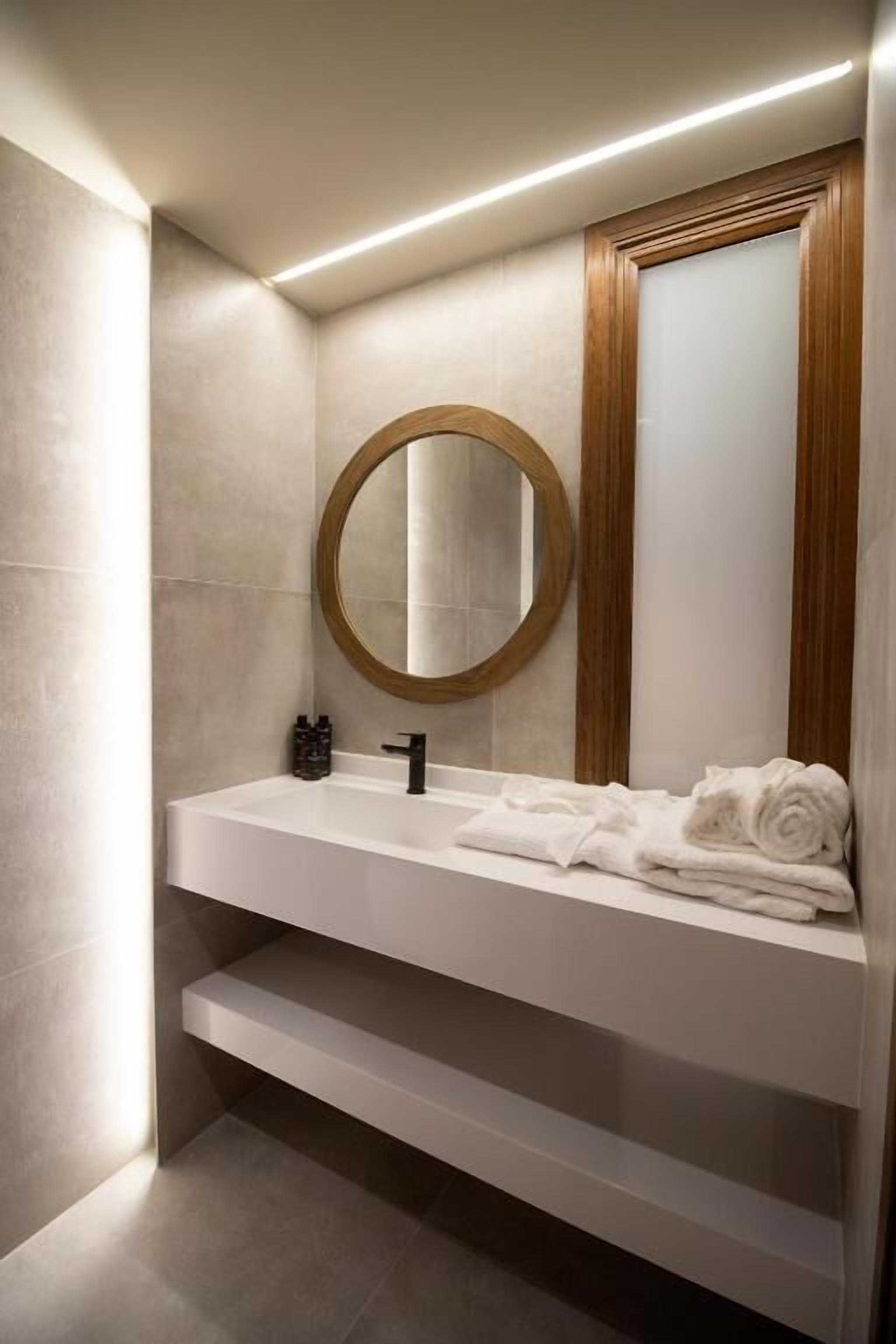 Une salle de bain moderne avec un meuble-lavabo blanc, un miroir rond et un porte-serviettes.