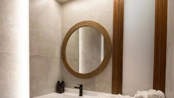 Une salle de bain moderne avec un meuble-lavabo blanc, un miroir rond et un porte-serviettes.