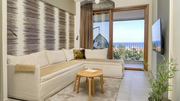 Una sala moderna con un sofá modular, una mesita de madera, un ventanal con vista a un edificio y una planta en maceta.