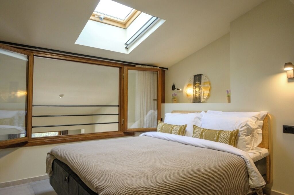A bedroom with a skylight, a bed with patterned bedding, a large mirror, and a wall-mounted light fixture.