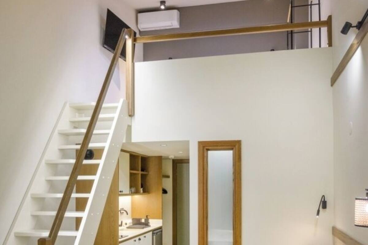 A bedroom with a bed, a sofa, a small table, a mirror, and a staircase.