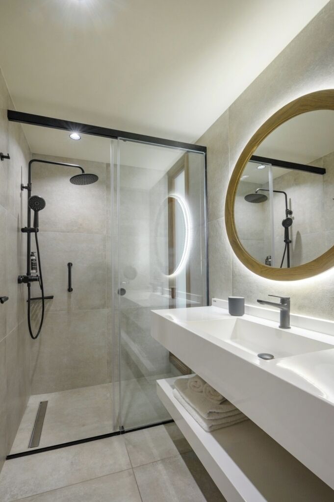Un bagno moderno con doccia vetrata, uno specchio grande e un mobile lavabo bianco.
