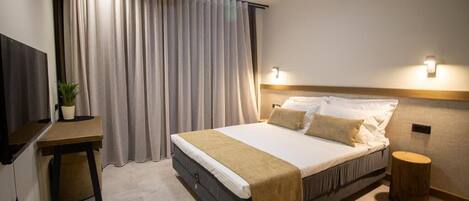 Une chambre à coucher comprenant un lit, un bureau, une chaise, une plante en pot, un ventilateur de plafond et un tabouret rond en bois.