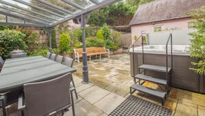 Een overdekt terras met een tafel, stoelen, een hottub en een houten bank.
