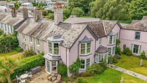 Een groot huis met veel erkers, een tuin met buitenmeubels en een verzorgd gazon.