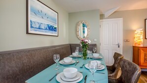 Un comedor con una mesa azul turquesa dispuesta para cuatro personas, un espejo y un cuadro en la pared.