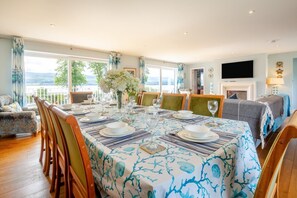 A dining area with a table set for six, chairs, a fireplace, and a TV mounted on the wall. - 5 Bed in Beaumaris (oc-s44705) (Beaumaris)