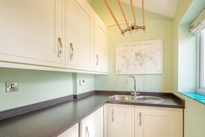 A kitchen with white cabinets, a black countertop, a stainless steel sink, and a world map on the wall. - 5 Bed in Beaumaris (oc-s44705) (Beaumaris)