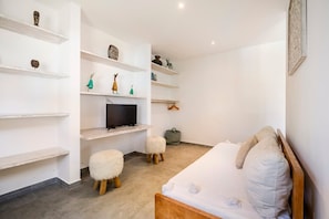 A bedroom with a bed, a TV, and shelves with decorative items. - Exquisite Architectural Villa with Outdoor Pool (Seminyak)