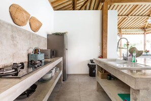 A modern kitchen with a stainless steel refrigerator, a microwave, and a sink. There are woven baskets on the wall and a wooden ceiling. - Exquisite Architectural Villa with Outdoor Pool (Seminyak)