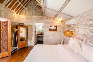 A rustic bedroom with a wooden ceiling, a bed with white linens, a wooden wardrobe, and a mirror. - Exquisite Architectural Villa with Outdoor Pool (Seminyak)