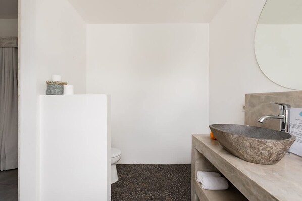 A modern bathroom with a stone sink, white toilet, and a mirror above the sink. - Exquisite Architectural Villa with Outdoor Pool (Seminyak)