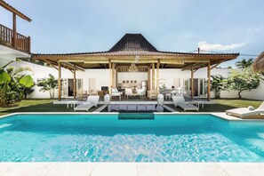 A poolside view of a house with a covered patio, a dining area, and a kitchen visible through the open space. - Exquisite Architectural Villa with Outdoor Pool (Seminyak)