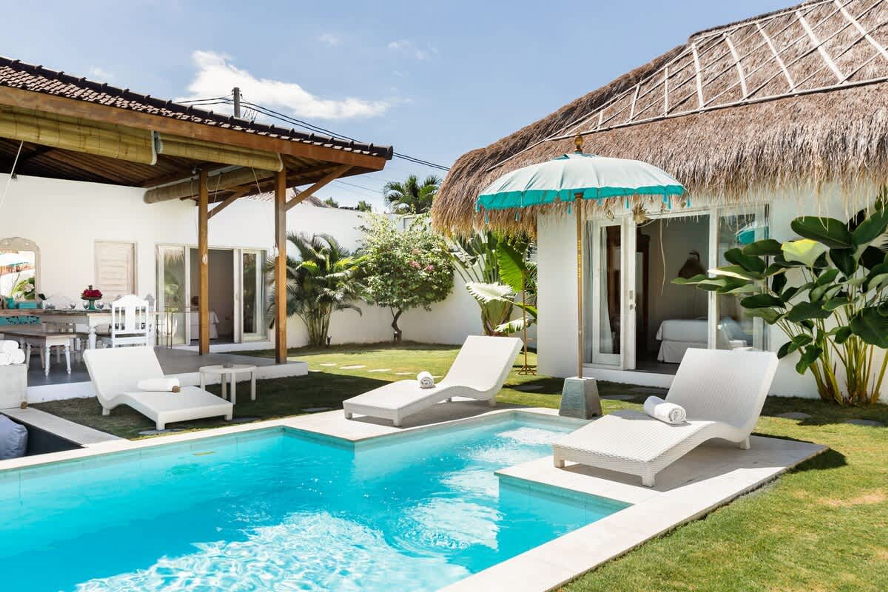 A swimming pool with lounge chairs, a thatched-roof structure, and a covered patio area.