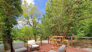An outdoor deck with wooden furniture, including chairs and tables, surrounded by lush greenery and trees. - 3 Bed in Llanrwst (oc-a43648) (Llanrwst)