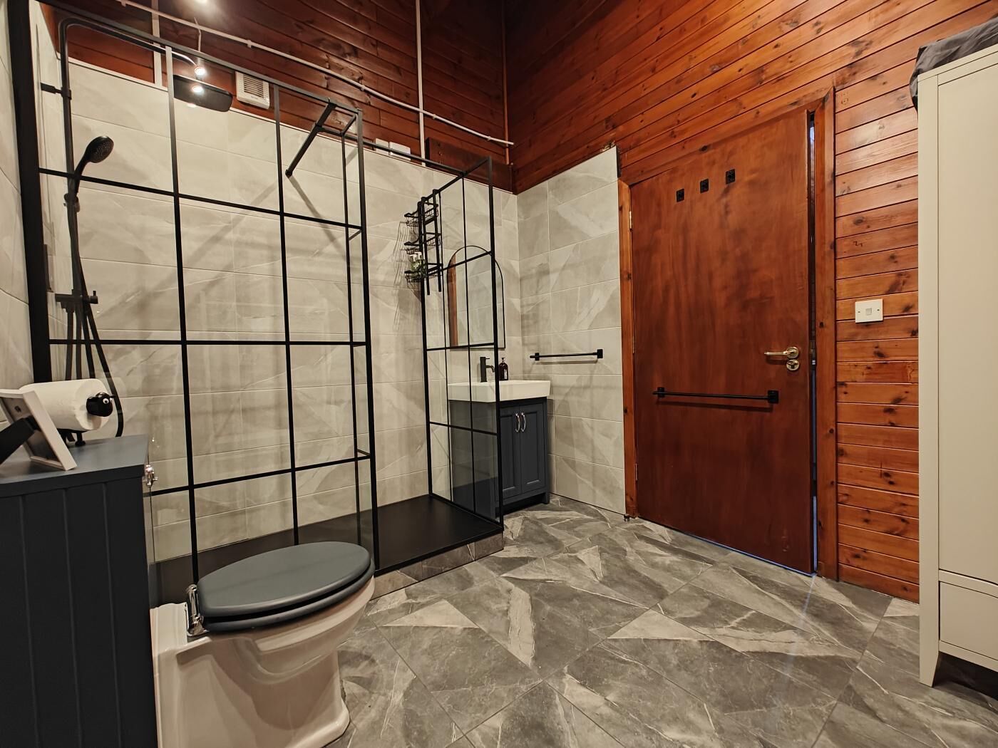 Une salle de bain avec douche, toilettes, lavabo et murs en bois.