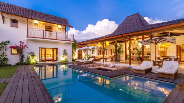 Una casa de dos plantas con piscina, mobiliario de exterior y un patio cubierto.