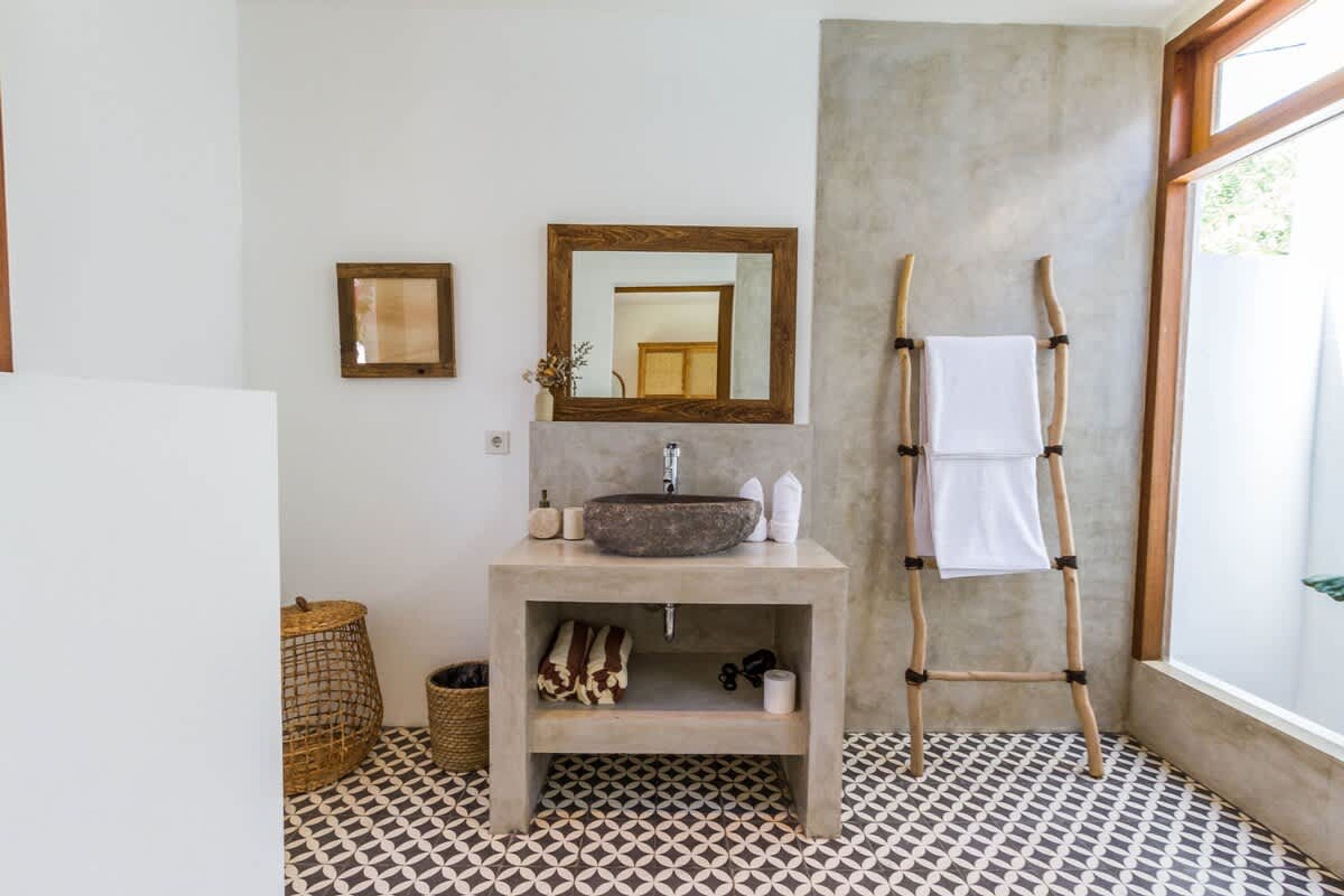 A bathroom with a stone sink, a wooden ladder, a mirror, and patterned floor tiles.