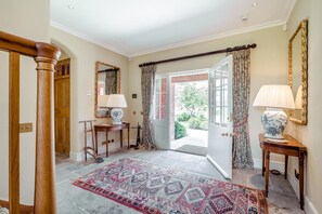 Un hall d’entrée avec un escalier en bois, un miroir, une table avec une lampe, des rideaux à motifs et un tapis.