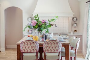 A dining area with a table set for four, surrounded by floral-patterned chairs. A vase with flowers is on the table, and there are plates and a pitcher on the table's surface. - 6 Bed in Chebbard (oc-c43267) (Puddletown)