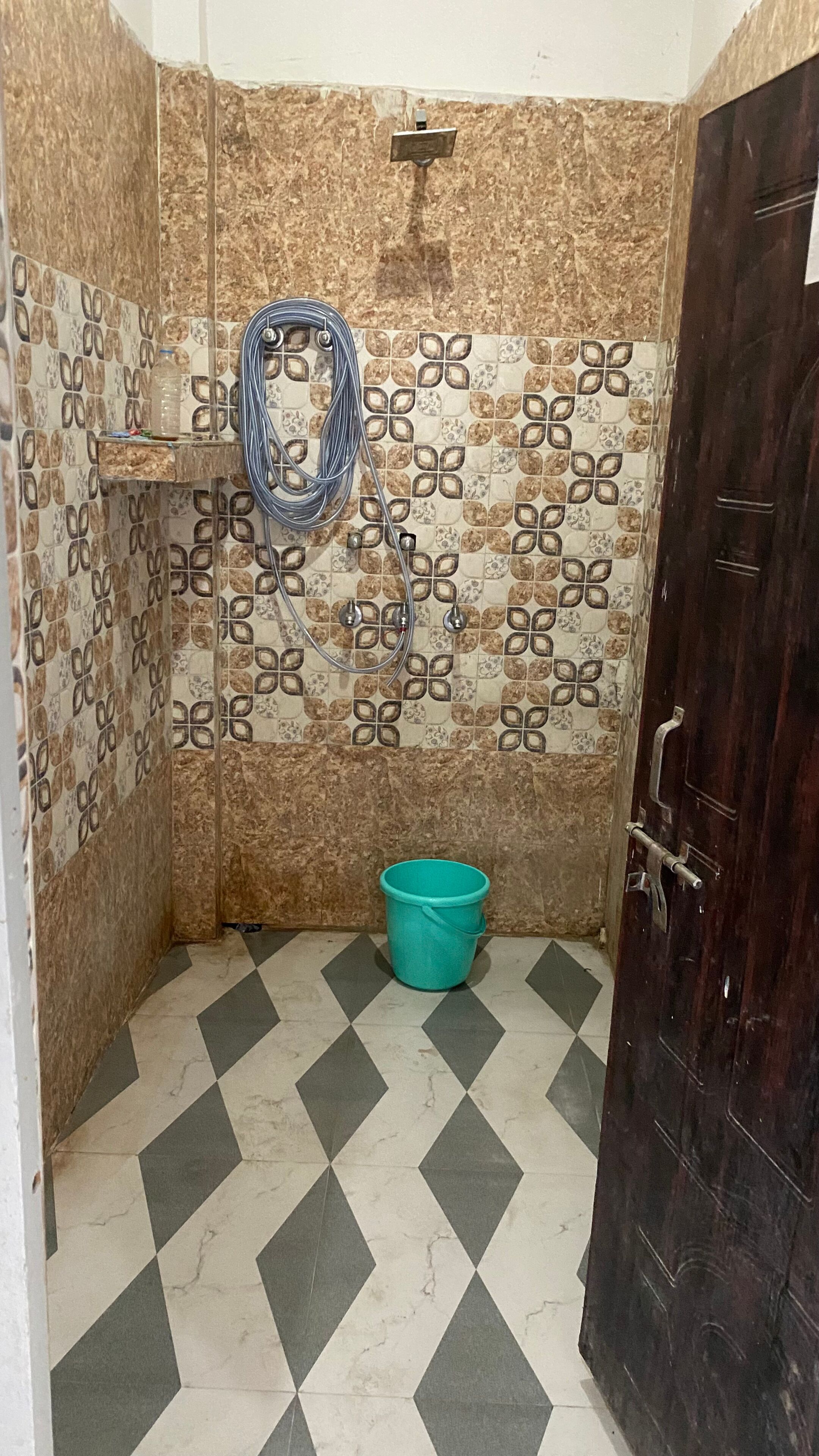 A bathroom with patterned walls, a tiled floor, a bucket, and a door.