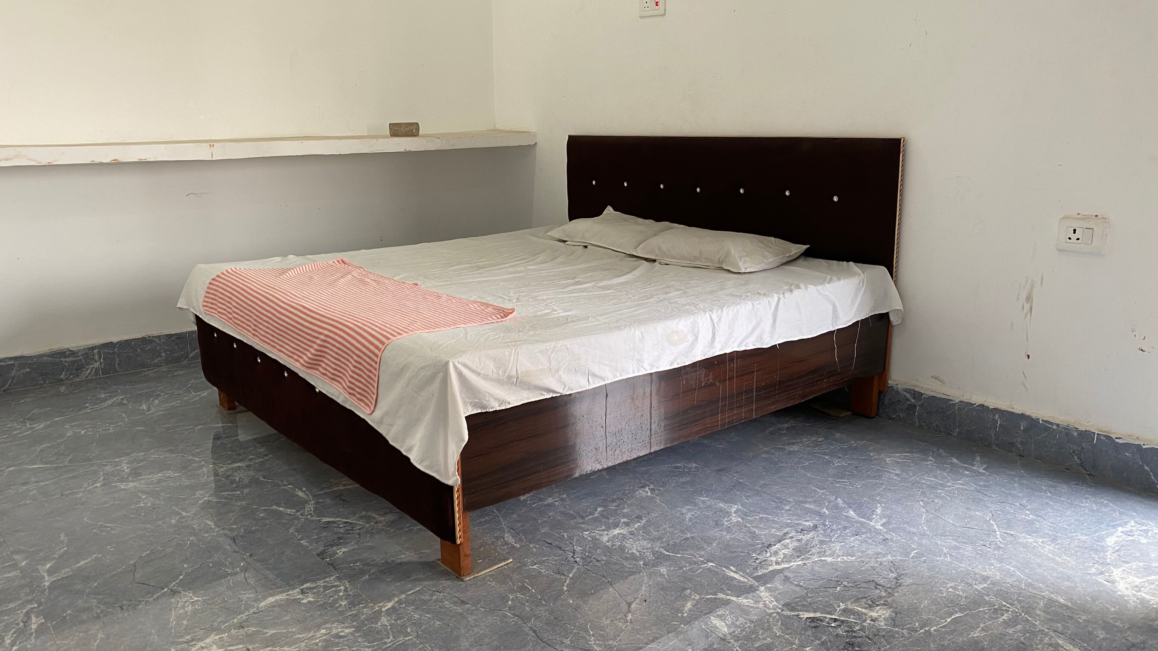Uma cama de solteiro com estrutura e cabeceira de madeira, uma colcha branca e um cobertor listrado.