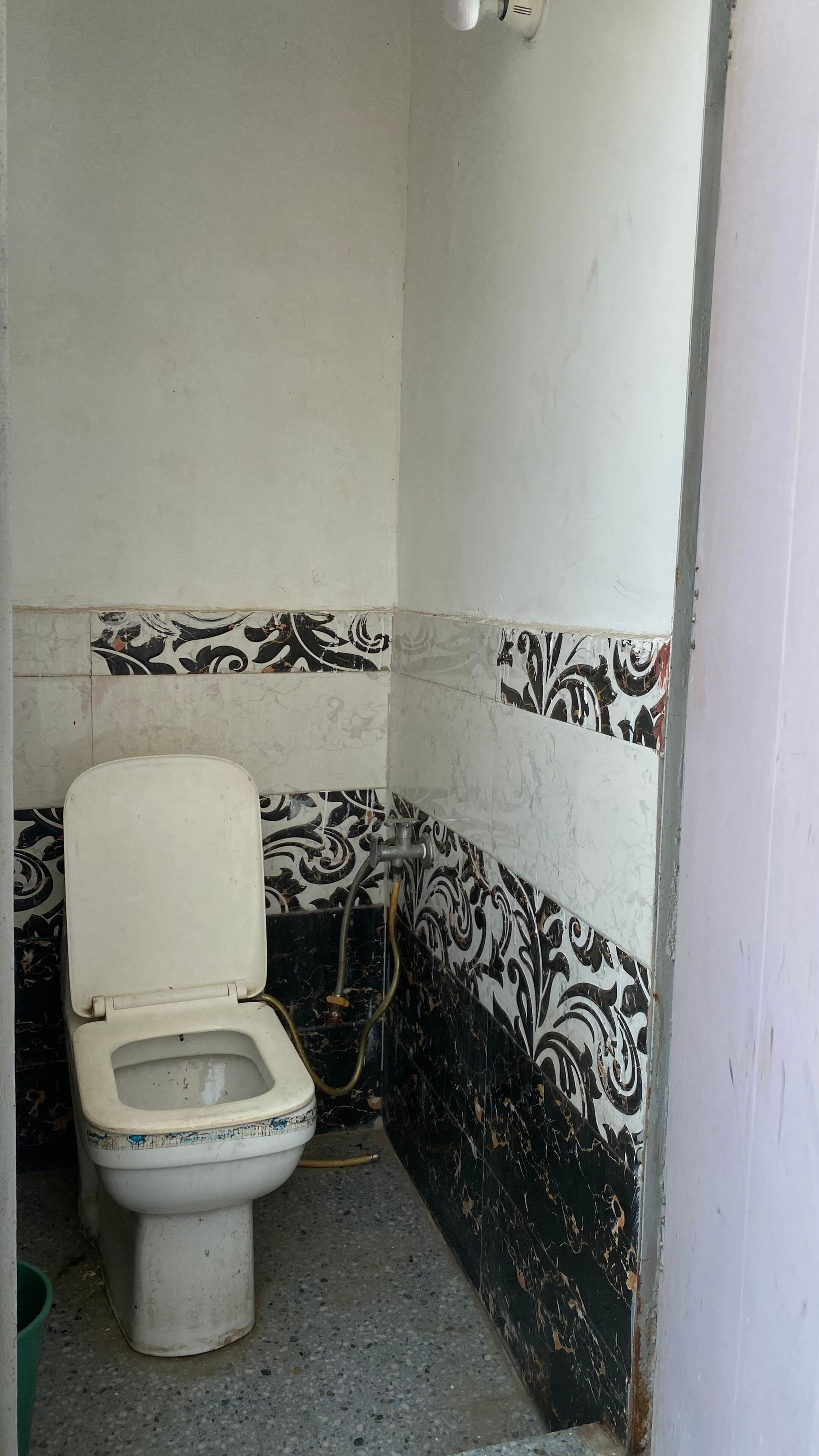 Een kleine, eenvoudige badkamer met toilet, wastafel en een wand met patroon betegelde tegels.