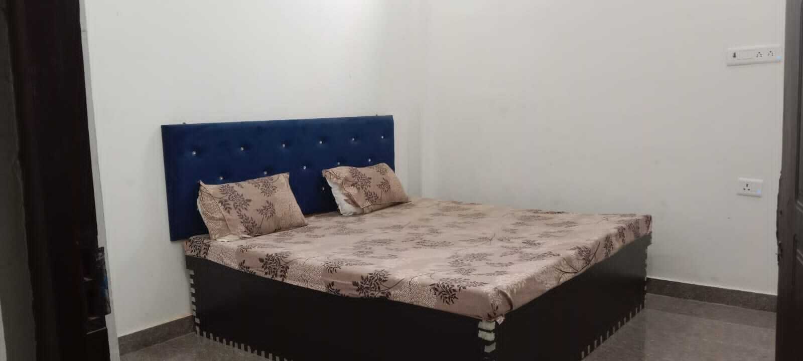 A bed with a blue headboard and floral bedding in a room with white walls and a tiled floor.