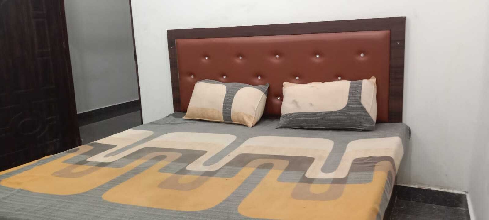 Una cama con cabecera capitonada, dos almohadas y una colcha estampada.